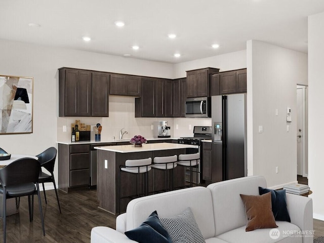 kitchen with a kitchen island, dark brown cabinetry, appliances with stainless steel finishes, and dark wood-style floors