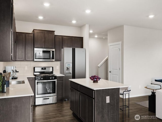 kitchen with a sink, a kitchen island, dark wood-type flooring, and appliances with stainless steel finishes