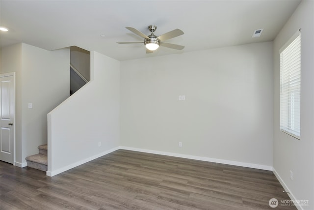 empty room with visible vents, baseboards, ceiling fan, stairs, and wood finished floors