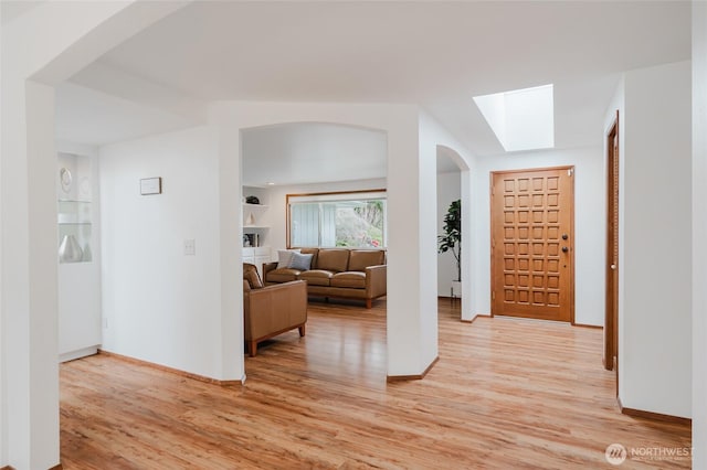 hallway with light wood-type flooring, arched walkways, baseboards, and a skylight