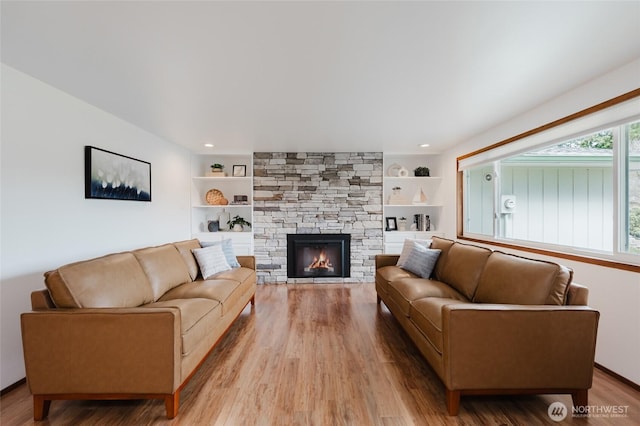 living room featuring built in features, recessed lighting, a stone fireplace, and light wood-style floors