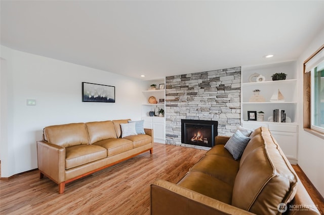 living room featuring a stone fireplace, built in shelves, recessed lighting, and light wood-type flooring