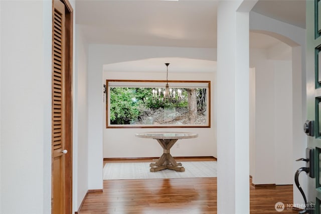 corridor with baseboards, arched walkways, a notable chandelier, and wood finished floors