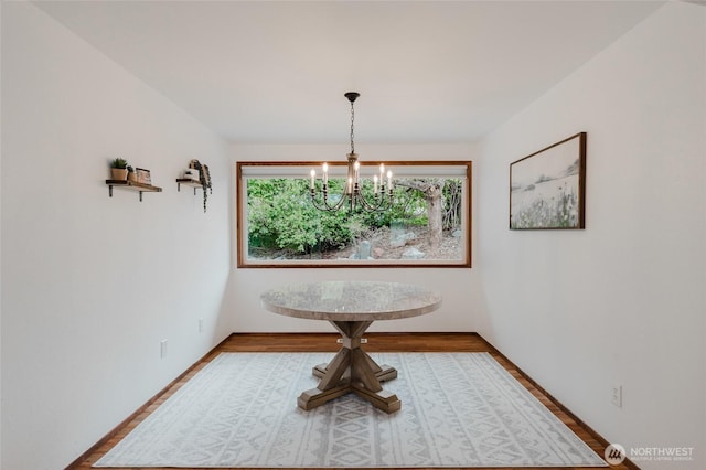 unfurnished dining area with a chandelier, baseboards, and wood finished floors