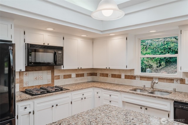 kitchen with black appliances, a sink, tasteful backsplash, white cabinetry, and light stone countertops