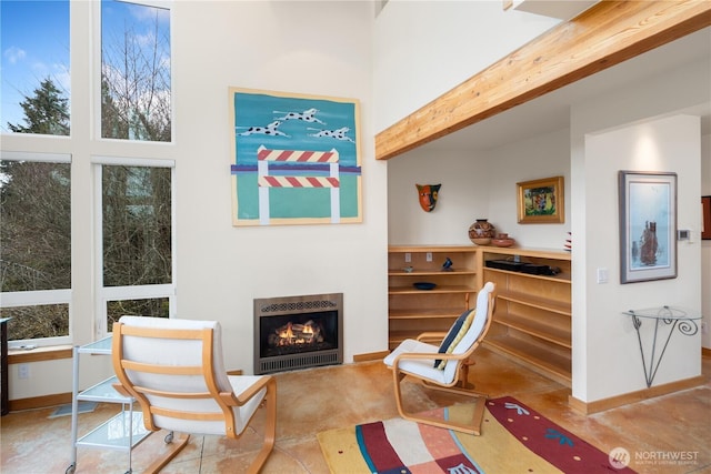 living area with heating unit, baseboards, beam ceiling, a high ceiling, and a warm lit fireplace