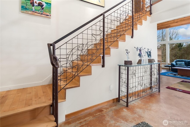 stairs with concrete flooring, baseboards, and a towering ceiling