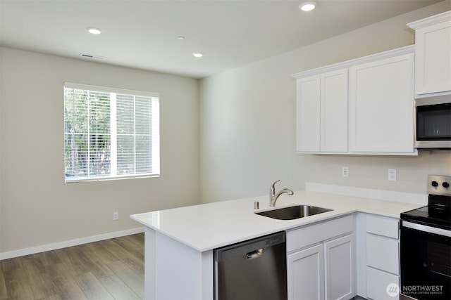 kitchen with a sink, a peninsula, white cabinets, and stainless steel appliances