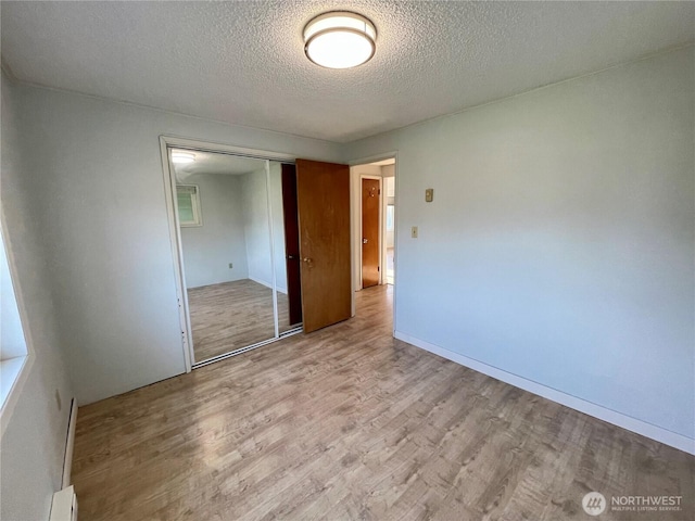 574 Ensign Ave NW, Ocean Shores, WA 98569 - unfurnished bedroom with a baseboard radiator, a textured ceiling, a closet, and wood finished floors