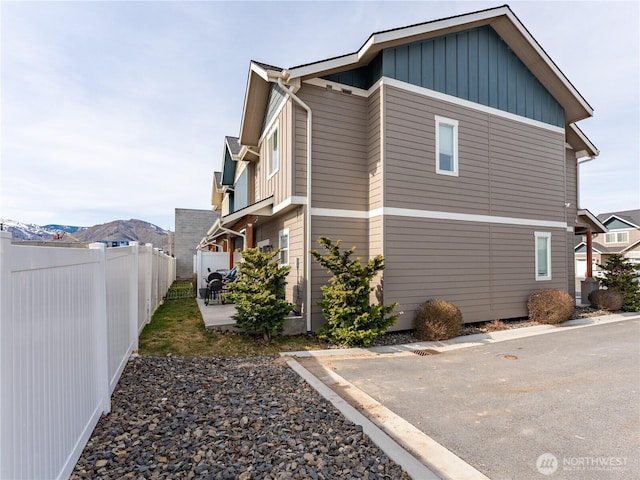 view of side of home featuring board and batten siding, a patio, fence, and a mountain view