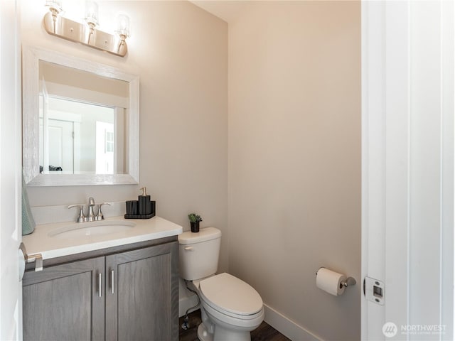 half bathroom with vanity, toilet, and baseboards