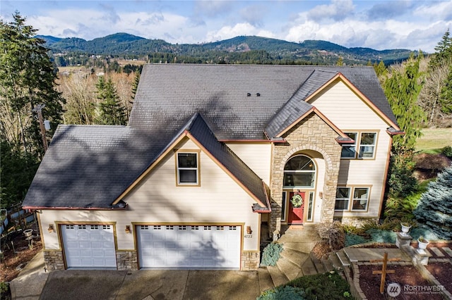 traditional-style home with a mountain view, an attached garage, stone siding, and driveway