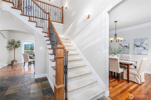 stairs with crown molding, baseboards, stone tile flooring, an inviting chandelier, and arched walkways