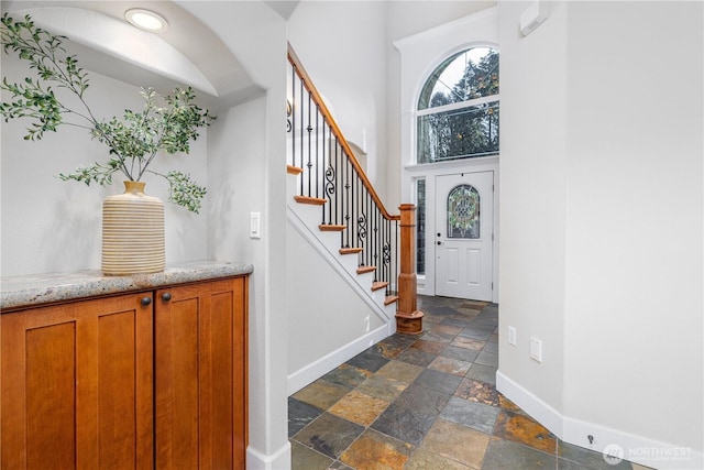 entrance foyer with stone tile floors, stairs, baseboards, and a towering ceiling