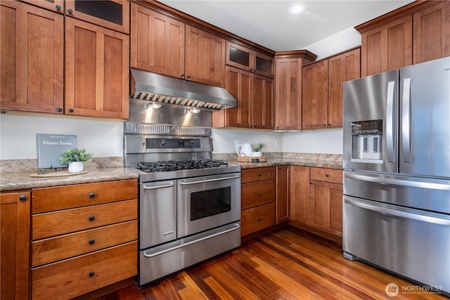 kitchen featuring dark wood-type flooring, brown cabinetry, under cabinet range hood, and stainless steel appliances