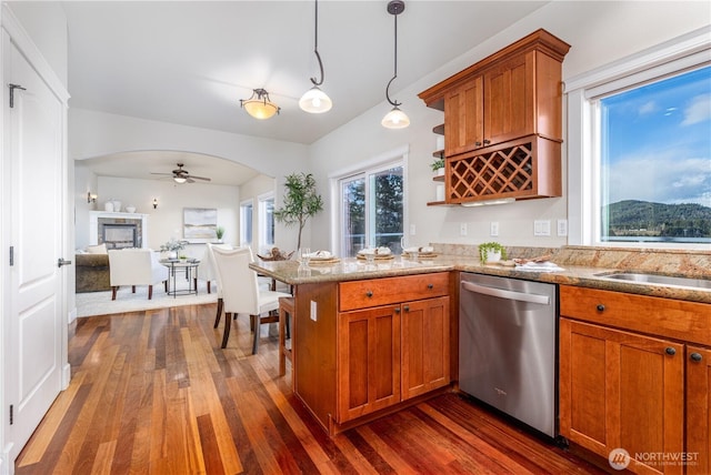 kitchen featuring light stone countertops, dark wood finished floors, dishwasher, brown cabinets, and a ceiling fan