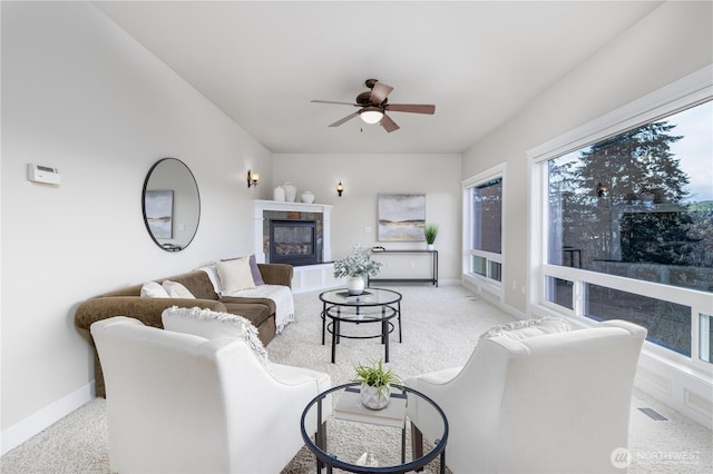 living room featuring light colored carpet, a tile fireplace, baseboards, and ceiling fan