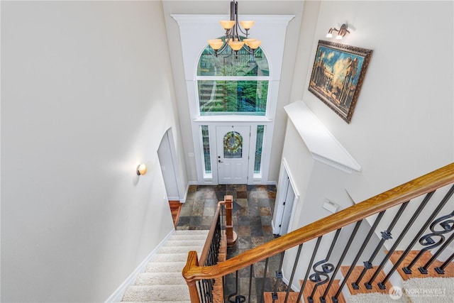 foyer entrance featuring stairway, baseboards, a high ceiling, stone finish flooring, and a notable chandelier