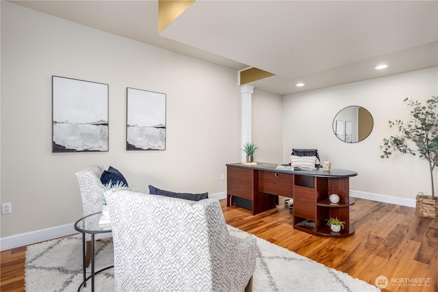 office space featuring light wood-type flooring, baseboards, and decorative columns