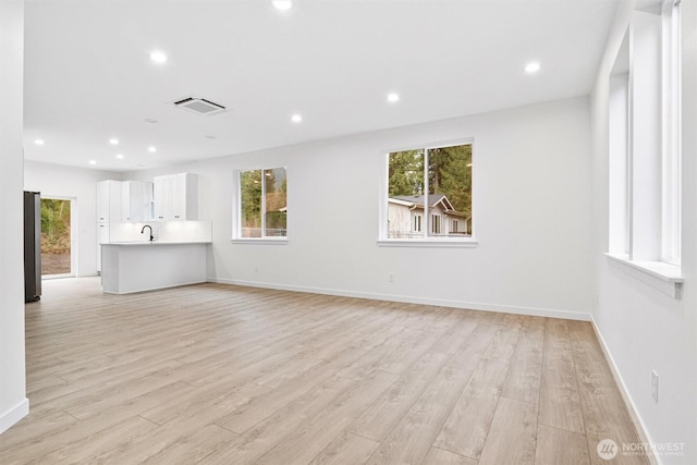 unfurnished living room with a wealth of natural light, visible vents, and light wood-style floors