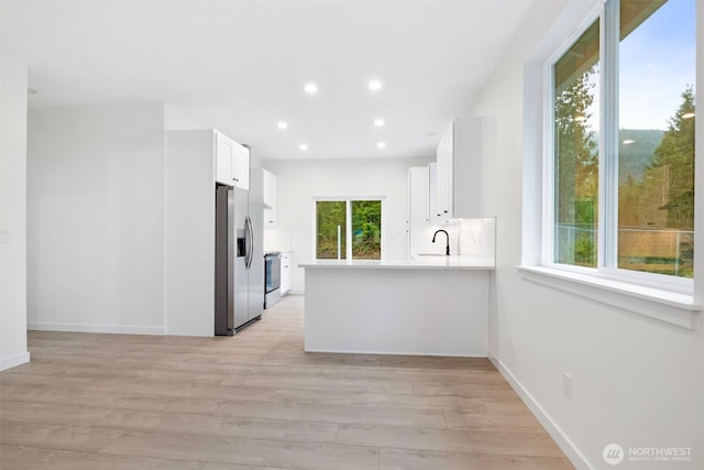 kitchen featuring a sink, electric range oven, light wood-style floors, stainless steel fridge with ice dispenser, and decorative backsplash