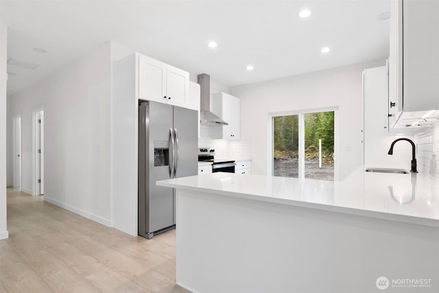 kitchen with backsplash, white cabinetry, appliances with stainless steel finishes, a peninsula, and wall chimney range hood