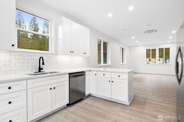 kitchen with dishwasher, light countertops, a peninsula, light wood-style floors, and a sink