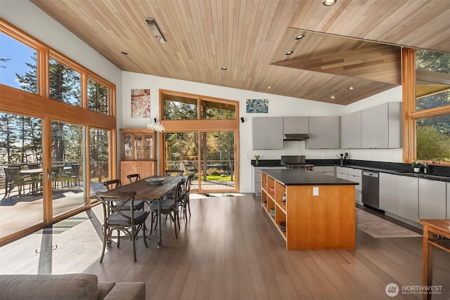 kitchen featuring dark countertops, a kitchen island, under cabinet range hood, dishwasher, and wood finished floors