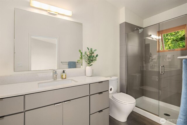 full bath with toilet, a stall shower, vanity, and wood finished floors
