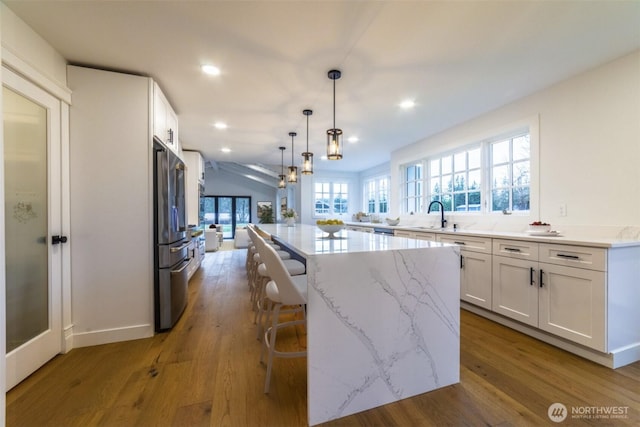 kitchen featuring white cabinets, wood finished floors, stainless steel fridge, and light stone countertops