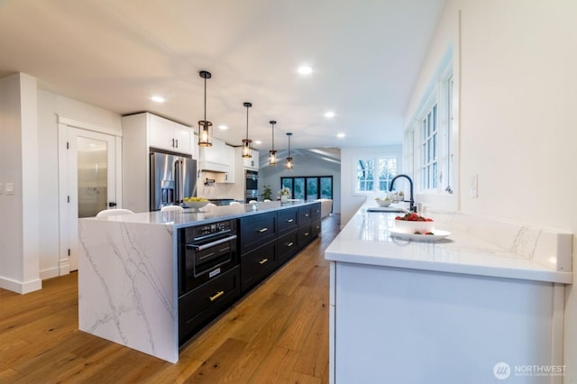 kitchen with a sink, dark cabinetry, light wood-style floors, and stainless steel appliances