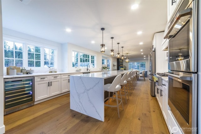 kitchen featuring a kitchen island, wine cooler, light stone counters, light wood-style floors, and white cabinetry