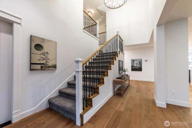 staircase with an inviting chandelier, a high ceiling, wood finished floors, and baseboards