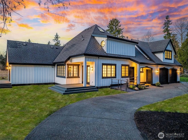 view of front of house with aphalt driveway, roof with shingles, covered porch, a garage, and a yard