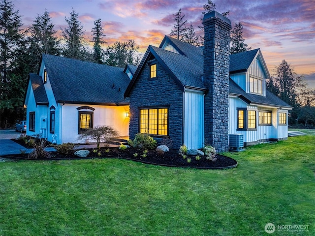 view of front of property featuring central air condition unit, a lawn, roof with shingles, and a chimney