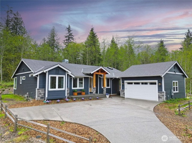 view of front facade featuring an attached garage, fence, stone siding, and driveway