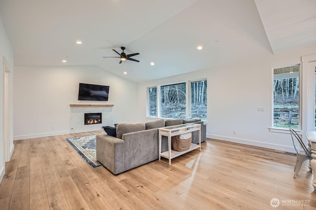 living area featuring a high end fireplace, light wood finished floors, baseboards, ceiling fan, and vaulted ceiling