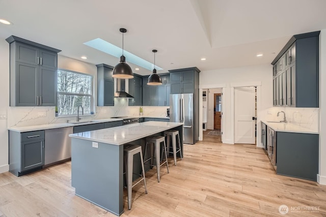 kitchen with a skylight, wall chimney exhaust hood, appliances with stainless steel finishes, and a sink