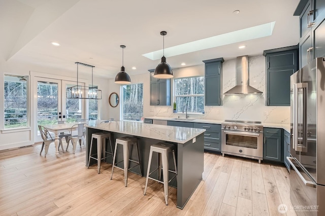 kitchen featuring a sink, premium appliances, tasteful backsplash, light wood-style floors, and wall chimney range hood