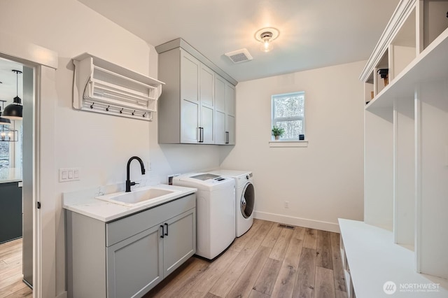 laundry area with visible vents, light wood-style flooring, cabinet space, independent washer and dryer, and a sink