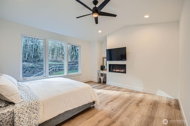 bedroom featuring baseboards, lofted ceiling, recessed lighting, wood finished floors, and a glass covered fireplace