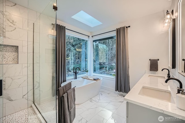 full bath featuring a sink, a freestanding tub, marble finish floor, and a skylight