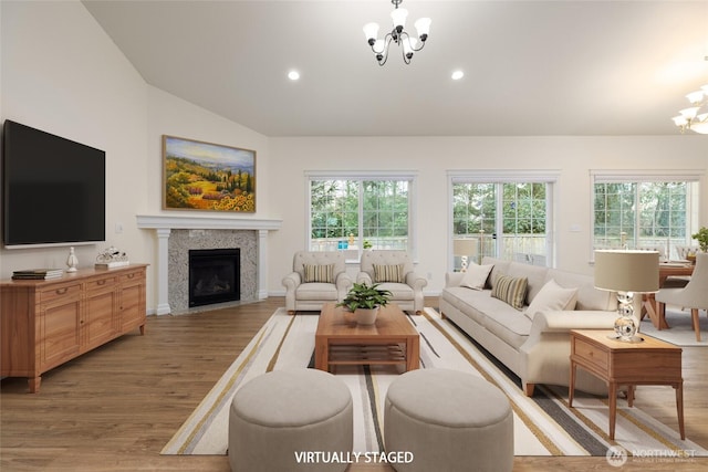 living area with plenty of natural light, a notable chandelier, light wood-style floors, and vaulted ceiling