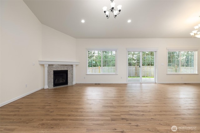 unfurnished living room with a fireplace with flush hearth, vaulted ceiling, wood finished floors, and a chandelier