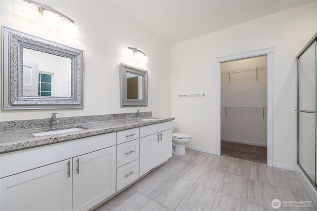 bathroom featuring double vanity, a sink, a stall shower, and a walk in closet