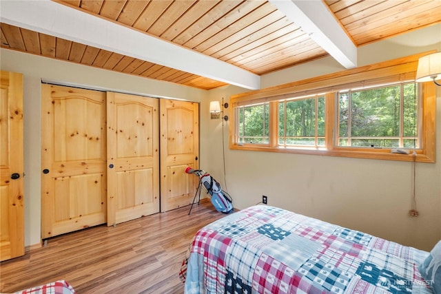 bedroom featuring beam ceiling, wooden ceiling, a closet, and light wood-style floors