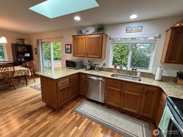 kitchen featuring light wood-type flooring, a sink, stainless steel appliances, a peninsula, and a skylight