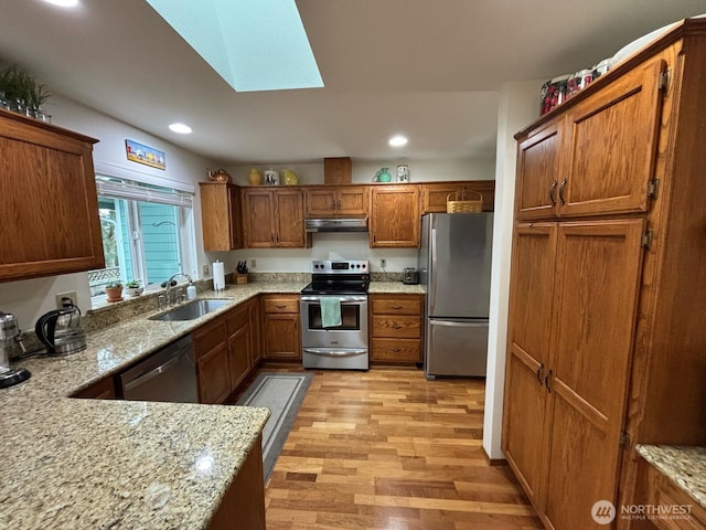 kitchen with light wood-type flooring, brown cabinets, a skylight, stainless steel appliances, and a sink