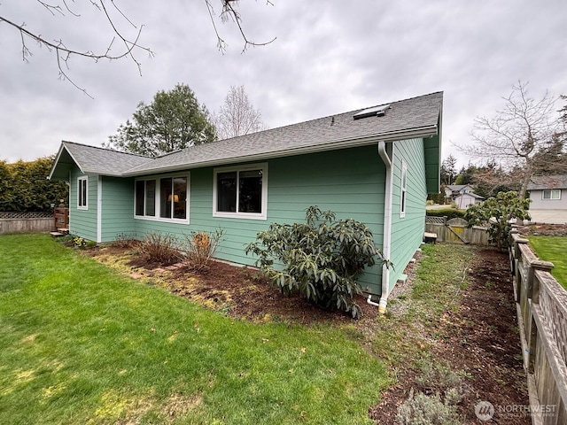 view of property exterior featuring a lawn, a shingled roof, and fence