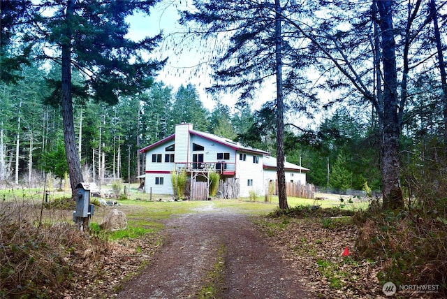 view of front of home with a forest view, a chimney, a deck, and dirt driveway